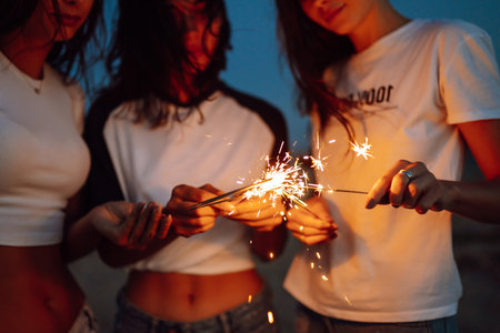The sparklers in the hands of young girls on the beach. Three girls enjoying party on beach with...