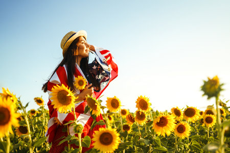 Beautiful girl in hat with the American flag in a sunflower field. 4th of July. Fourth of July. Freedomの写真素材