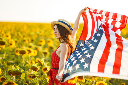 Beautiful girl in hat with the American flag in a sunflower field. 4th of July. Fourth of July. Freedomの写真素材
