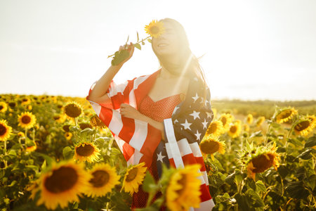 Beautiful girl in hat with the American flag in a sunflower field. 4th of July. Fourth of July....