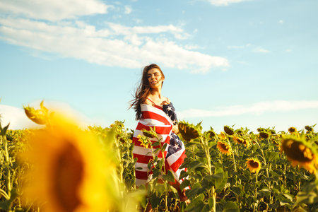 Beautiful girl in hat with the American flag in a sunflower field. 4th of July. Fourth of July. Freedomの写真素材