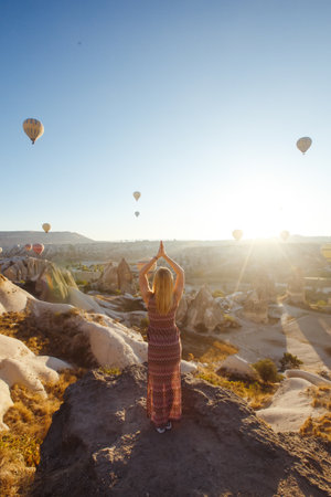 Young attractive girl stands on the mountain with flying air balloons. view from the back. cappadocia.の写真素材