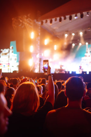 People taking photograph with phone during music festival Fans enjoying rock concert with light showの写真素材