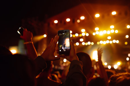 People taking photograph with phone during music festival Fans enjoying rock concert with light showの写真素材