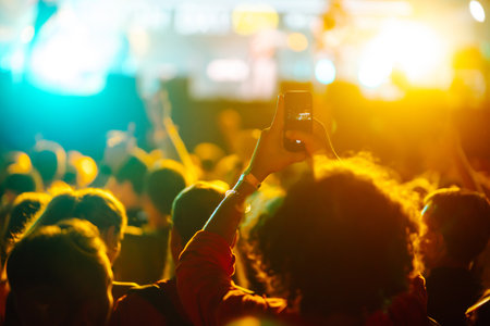 People taking photograph with phone during music festival Fans enjoying rock concert with light showの写真素材