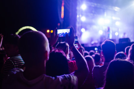 People taking photograph with phone during music festival Fans enjoying rock concert with light showの写真素材