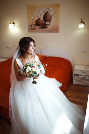 Morning of the bride. Beautiful smiling brunette bride in a white dress with a wedding bouquet in her hands.の写真素材
