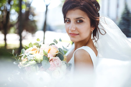 Beautiful bride with a wedding bouquet for a walk in the park. Young bride in white dress. wedding day. Marriageの写真素材