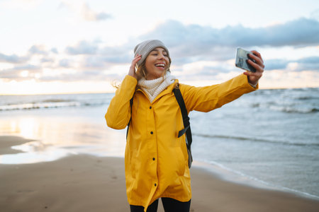 Tourist with phone. selfie time. Tourist in yellow jacket posing by sea at sunset. Travelling.