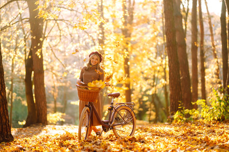 Stylish woman with a bicycle enjoying autumn weather in the park. Beautiful woman in the autumn forest.の写真素材