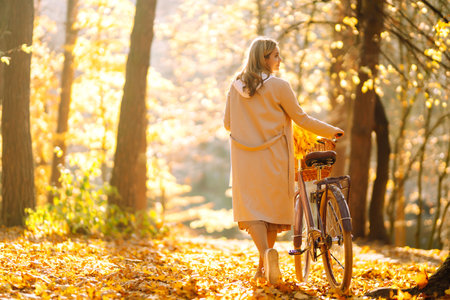 Stylish woman with a bicycle enjoying autumn weather in the park. Beautiful woman in the autumn forest.の写真素材