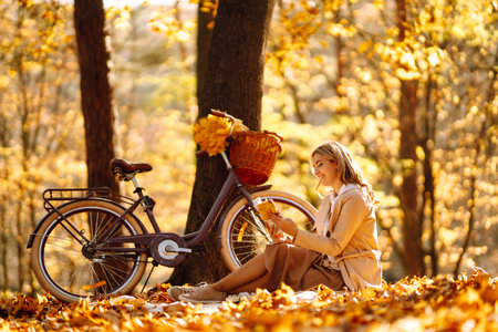 Beautiful young woman sitting on a fallen autumn leaves in a park, reading a book. relaxation.の写真素材