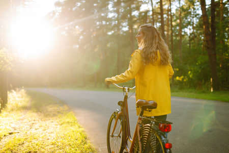 Young happy woman in yellow coat rides bicycle in sunny park. Relax, nature concept. lifestyle.の写真素材