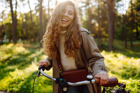 Smiling woman with curly hair in coat rides bicycle in sunny park. lifestyle. Relax, nature concept.の写真素材