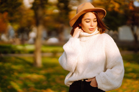 autumn woman. Young cheerful woman in white sweater and hat walks in the nature park on a sunset.の写真素材
