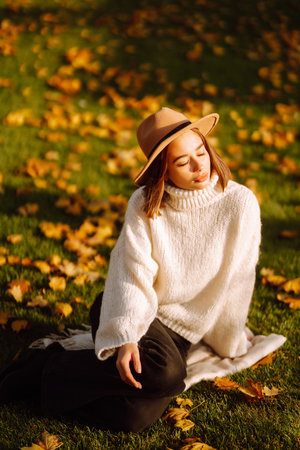 autumn woman. Young cheerful woman in white sweater and hat walks in the nature park on a sunset.の写真素材