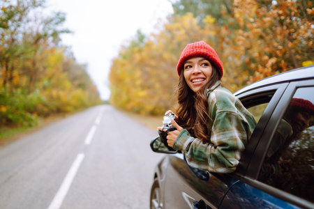 Beautiful woman takes pictures on camera from the car window. Rest, relaxation, lifestyle concept.の写真素材