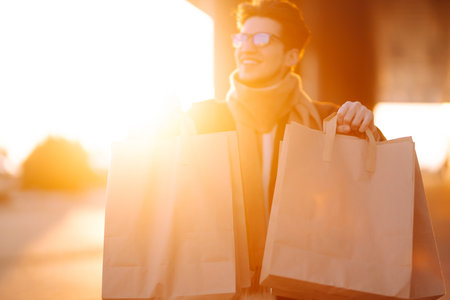 Stylish man with paper packages after shopping at sunset. Handsome man doing shopping.の写真素材