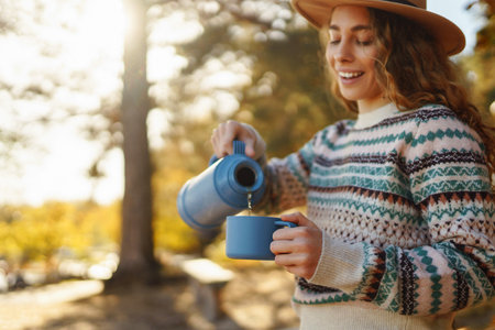 Woman holds and drinks tea in sunny autumn forest. Vacation, travel, lifestyle concept.の写真素材