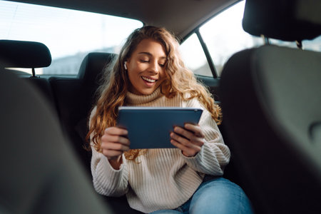 Young woman sitting in back seat of car with tablet in hand. Business, technology, online concert.の写真素材