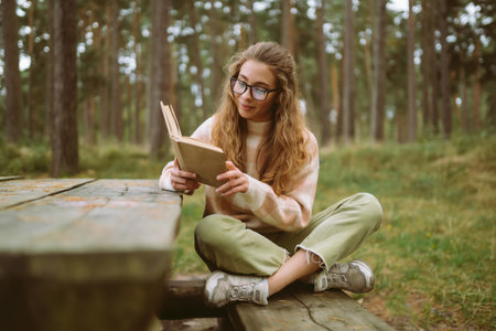 Happy woman is sitting at table with book in beautiful forest. Concept of relaxation, lifestyle.の写真素材
