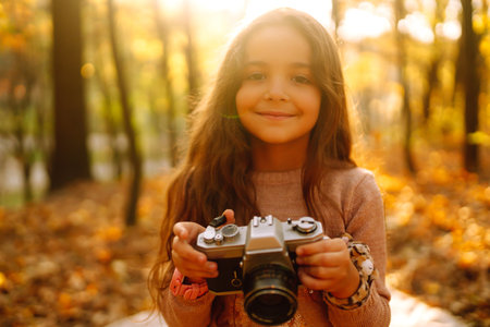 A little girl having fun in the autumn forest with retro camera. Happy child playing in the autumn