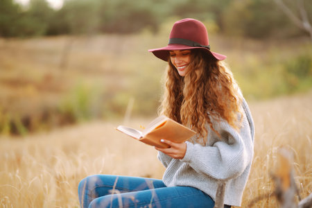 Fall picnic in nature. Young woman sitting on the blanket reading a book and smiling outdoors.の写真素材