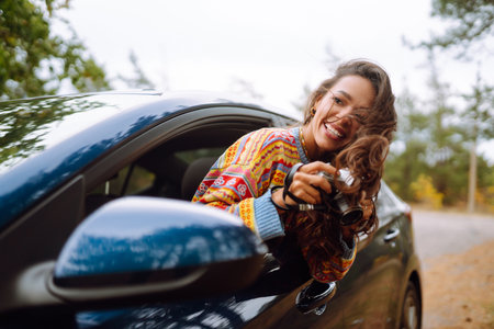 Happy woman takes pictures on camerafrom car window Enjoying autumn weather. Rest, lifestyle conceptの写真素材