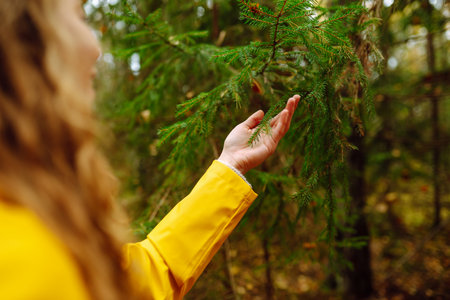 Traveler woman in yellow coat explores, walks through wild forest in nature. Vacation travel conceptの写真素材
