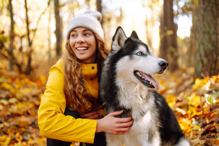 Smiling woman in a yellow coat walks with her cute pet Husky in the autumn forest in sunny weather.の写真素材