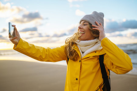 Tourist with phone. selfie time. Tourist in yellow jacket posing by sea at sunset. Travelling.の写真素材