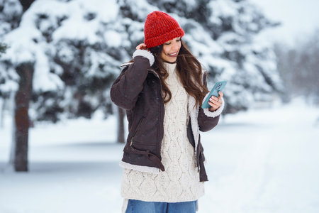 Happy woman in a red hat with a phone takes a selfie, blogs in the winter forest. Concept of nature.