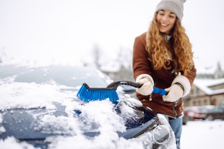 Beautiful woman is cleaning snow from a car with a brush. Transport concept, seasonalityの写真素材