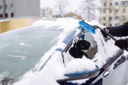 Young man cleaning snow from car with brush. Transport, winter, weather, people and vehicle concept.の写真素材