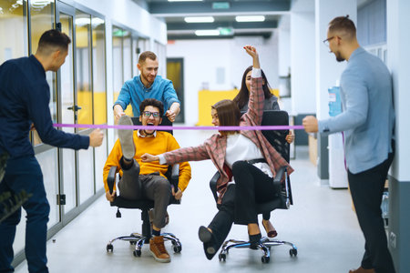 Young cheerful business people racing on office chairs and laughing. Funny activity