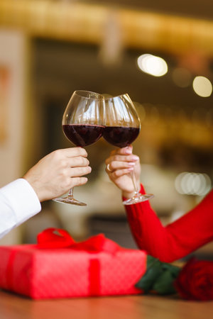 Couple click glasses with red wine. Lovers give each other gifts. Lovely romantic dinner.の写真素材