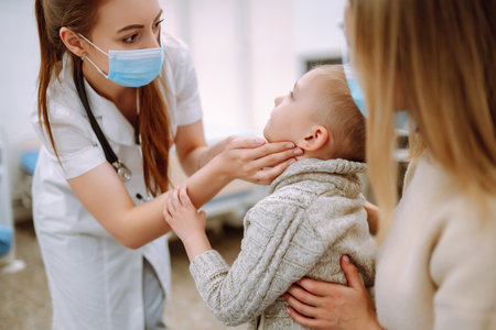Pediatrician examines sick boy. Child with his mother in the office of pediatrician or otolaryngologist.の写真素材