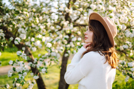 Portrait of Beautiful Woman In hat posing near flowering. Smiling woman enjoying the smell of flowers.の写真素材