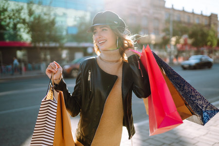 Smiling woman with shopping bags using her phone. Young woman after shopping on the city street.