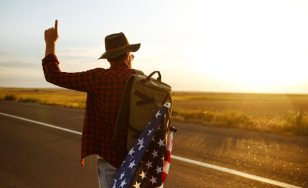 4th of July. American Flag. Traveler with the flag of America. The man in a hat, a backpack, a shirt and jeans.の写真素材