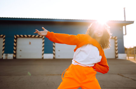 Young African American woman - dancer dancing in the street at sunset. Stylish woman with curly hair...
