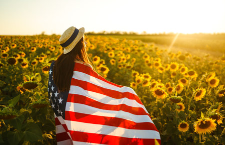 Beautiful girl in hat with the American flag in a sunflower field. 4th of July. Fourth of July. Independence Day.の写真素材