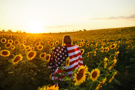 Beautiful girl with the American flag in a sunflower field. 4th of July. Fourth of July. Freedom