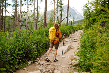 Stylish tourist woman with yellow backpack against backdrop of mountain scenery. Concept of travel.