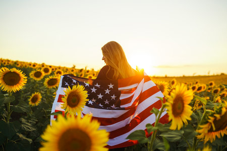 Beautiful girl with the American flag in a sunflower field. 4th of July. Fourth of July. Freedom
