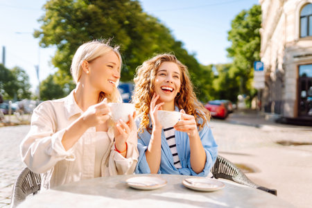 Portrait of a smiling young women friends sitting outdoors in cafe drinking coffee. Beauty, relax.の写真素材