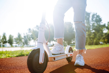 Young female legs on electric scooter. Woman rides electric scooter in park. Active lifestyle.の写真素材