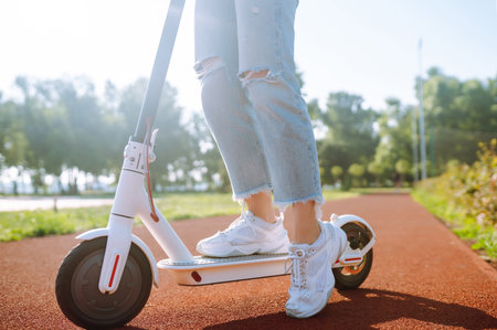 Young female legs on electric scooter. Woman rides electric scooter in park. Active lifestyle.の写真素材