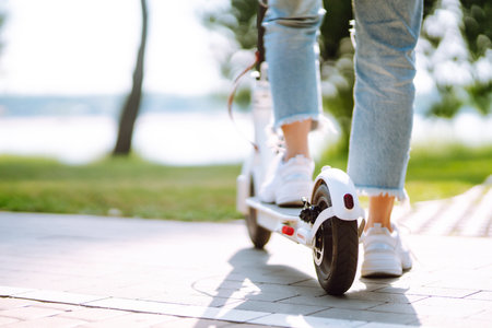 Young female legs on electric scooter. Woman rides electric scooter in park. Active lifestyle.の写真素材
