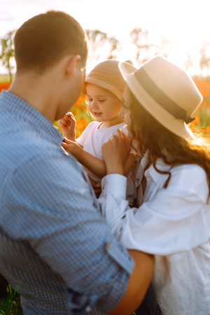 Family with a child walking on a poppy field. Mother, father, little daughter having fun on the poppy field.の写真素材